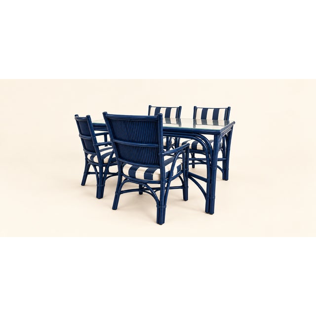 A striking rattan dining set featuring a rectangular glass-top table and four coordinating chairs, all presented in a rich...