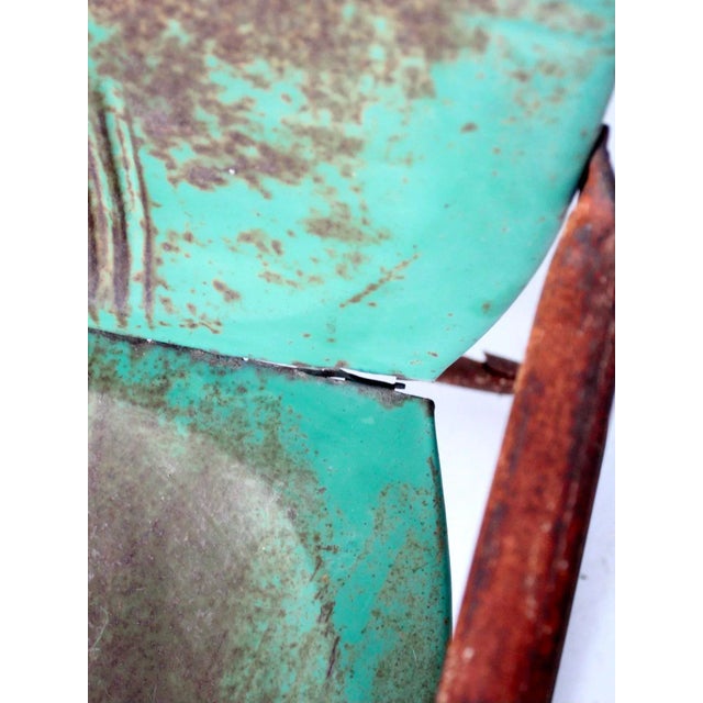 A mid-century metal patio chair with a classic “bouncer” frame and a soft green finish. The surface shows a beautifully...