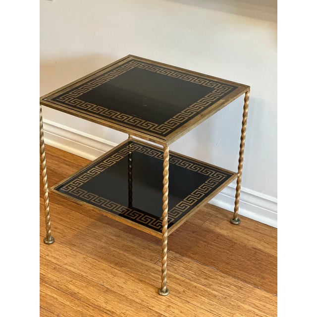 A refined mid-century side table featuring a gilt iron frame with twisted legs and a striking Greek key motif etched into...