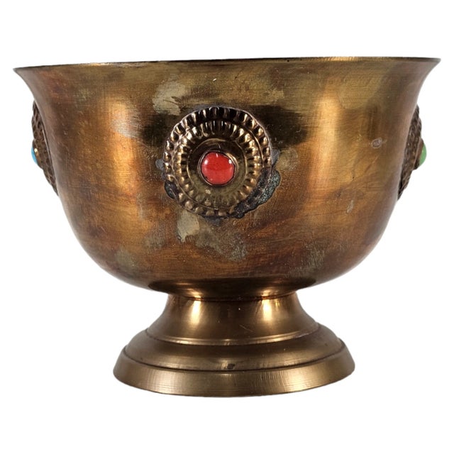 A Tibetan temple vessel of deep resonance, crafted in bronze and adorned with inset green and red stones, each set within...
