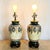 This elegant pair of hand-painted table lamps features rich green, gold, and cream tones with ornate floral motifs and...
