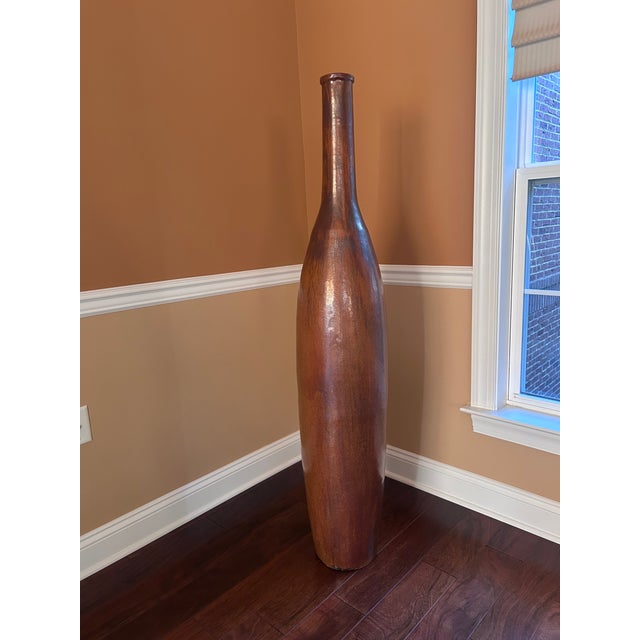 Monumental handcrafted sculptural floor vase with an elegant elongated bottle silhouette and rich warm brown finish. This...