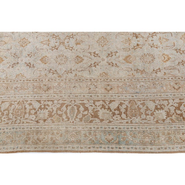 This early 20th century antique Persian rug features all-over beige floral abstractions over a field of ice blue. The...