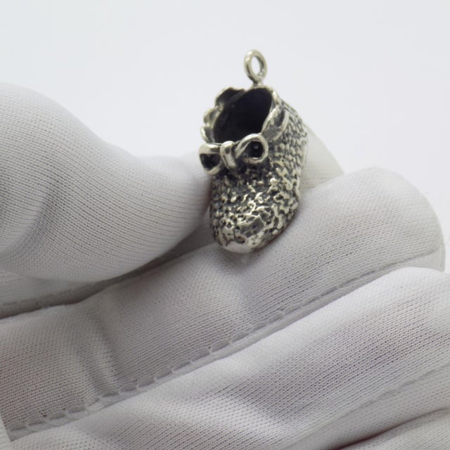 This delicate miniature pendant depicts a detailed newborn shoe, handcrafted in Arezzo, Tuscany during the 1970s/1980s....