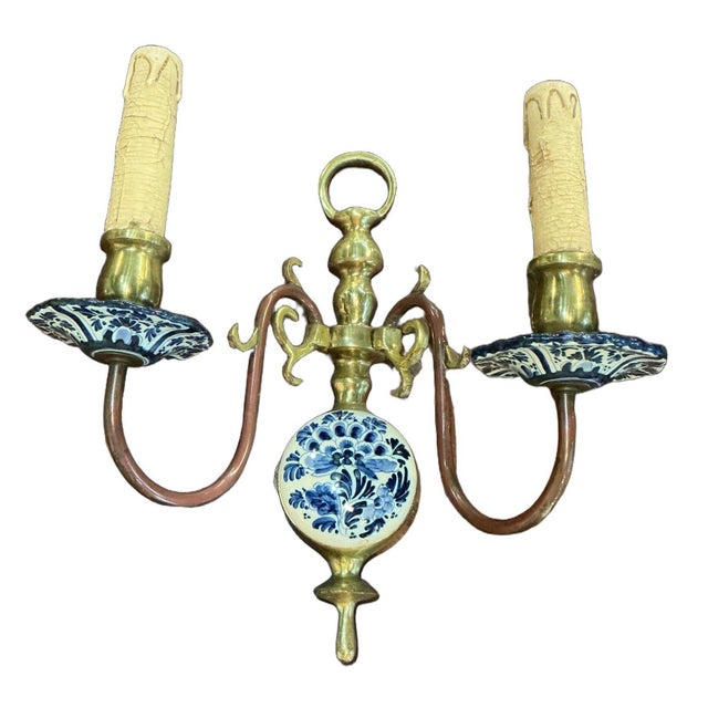 Beautiful pair of hand painted delft wall sconces. They feature a central brass stem with a hanging loop at the top. A...