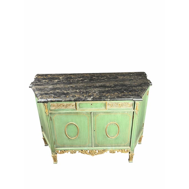 sideboard or buffet featuring a soft green painted finish accented with elegant gold detailing throughout. The cabinet is...
