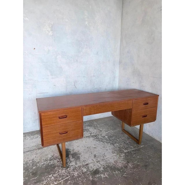 A distinctive mid-century teak desk with a floating twin-pedestal arrangement and sculptural sleigh-leg supports. Five...