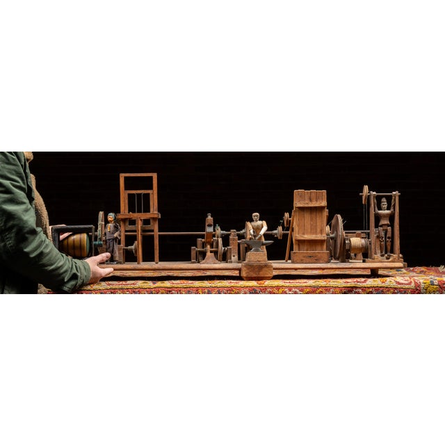 Antique hand-operated mechanical sideshow or fair model depicting an active blacksmith and forge workshop. The elongated...