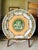 A beautiful antique transferware plate featuring a classical cherub scene at the center, surrounded by an elegant...