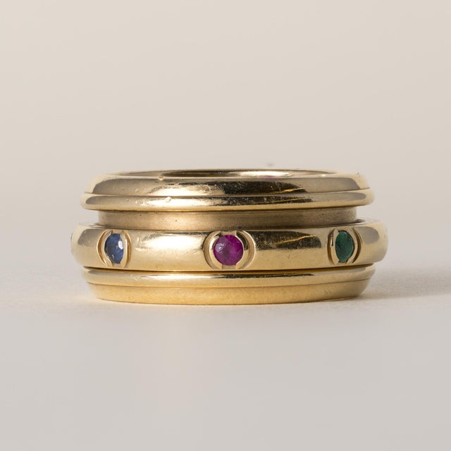 An iconic vintage Piaget Possession spinner ring in 18K yellow gold, featuring a rotating band set with emeralds, rubies,...