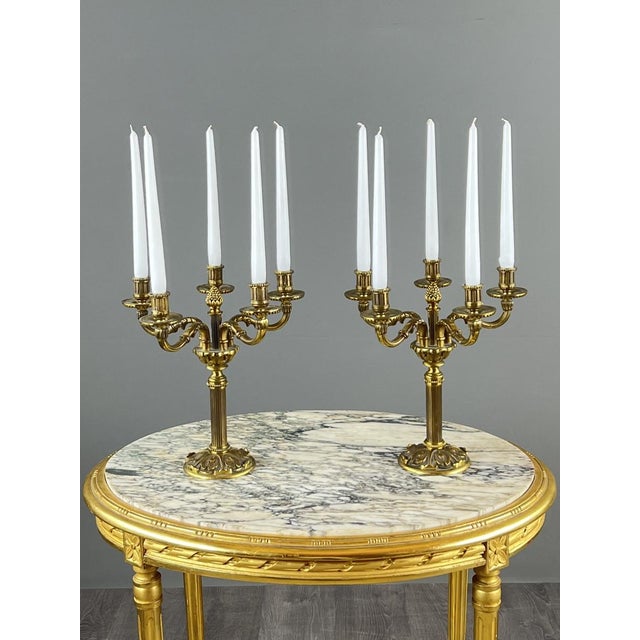 An elegant pair of gilt bronze candelabra with refined neoclassical-inspired decoration. Each piece features five finely...