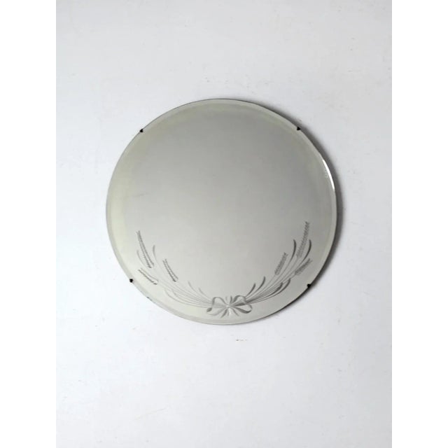 An antique round etched glass mirror with refined Art Deco detailing. The design features a delicate ribbon and wheat...