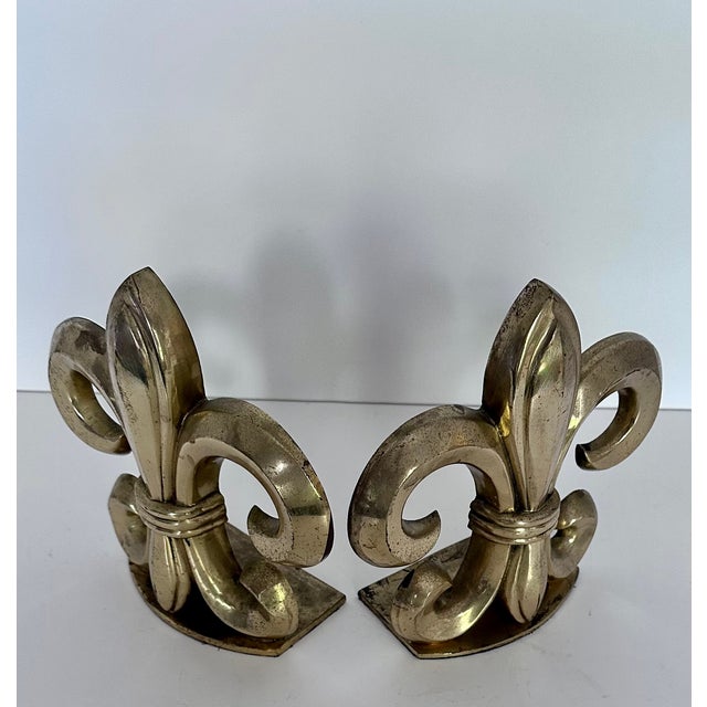 A pair of cast brass fleur de lis bookends, on cast iron bases. Dated to 1960s/70s. There is light age and use wear to the...