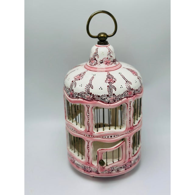 A whimsical French porcelain birdcage featuring an elegant domed top surmounted by a brass ring handle. The cage is...