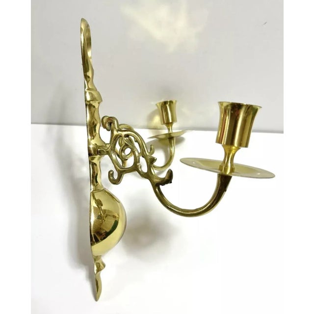 A decorative pair of vintage brass wall candle sconces with graceful scrolling arms, pierced scrollwork, and two taper...
