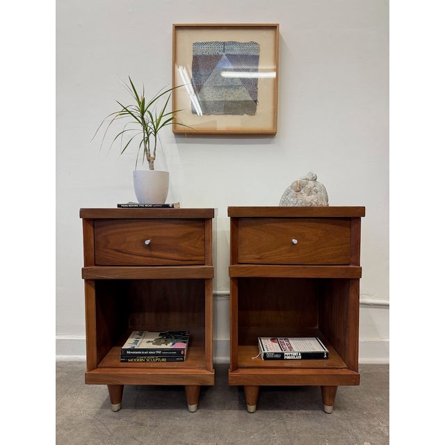 Pair of refurbished vintage walnut nightstands featuring clean mid-century lines, a single drawer for storage, and an open...
