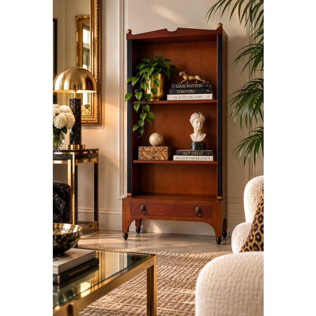 Elegant 1960s Hollywood Regency bookcase in the style of Baker Furniture, featuring a warm wood finish accented with...