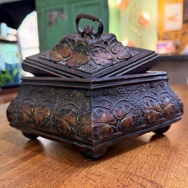 Intricately carved resin jewelry box features a rich dark wood-look finish with ornate floral and leaf motifs. The square,...