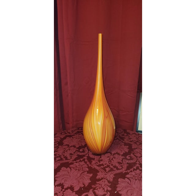 A striking mid-century modern tall art glass floor vase featuring rich orange, amber, and golden-yellow swirl striations....