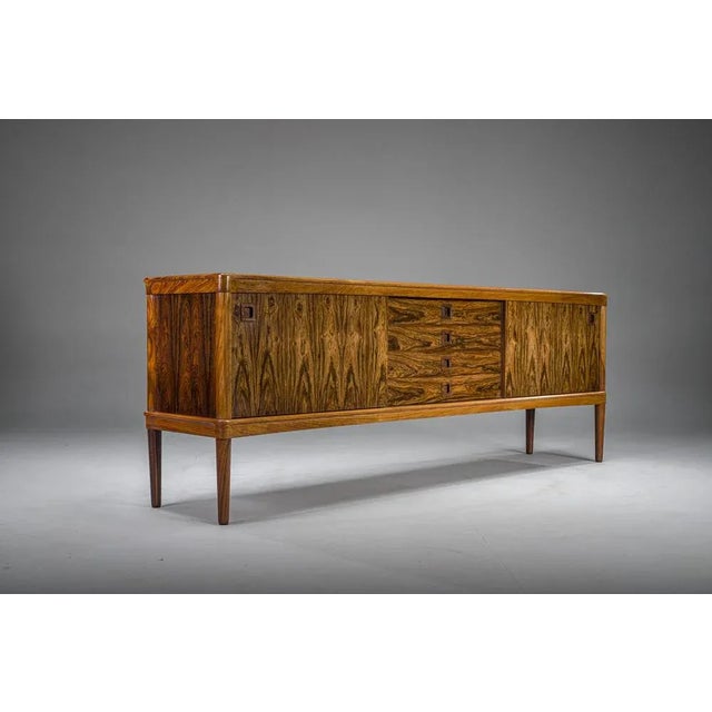 This is a rare and exquisitely preserved palisander rosewood sideboard, designed by hw klein for the esteemed danish...