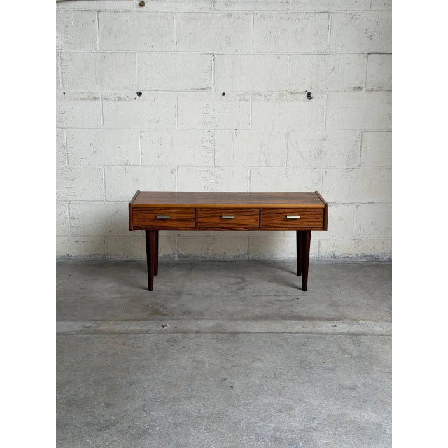 This elegant low-profile Entry Table features a long rectangular top elevated by beautiful tapered legs. Three side-by-...