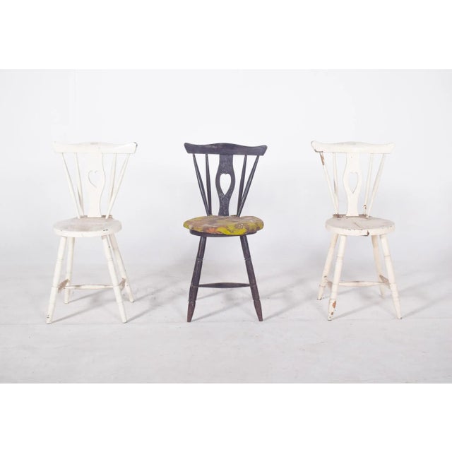 Three chairs with codtail backs. Painted wood, with cut-out backs and a hollowed-out ‘heart’ silhouette, evoking a...