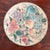 A hand-painted porcelain plate with peaches, grapes, pomegranates, and a small bird among leaves. The colors are soft...