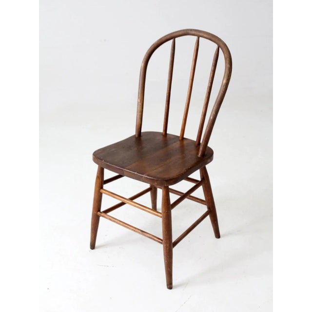 An antique farmhouse Windsor dining chair featuring a painted wooden frame, gracefully bowed back, and traditional turned...