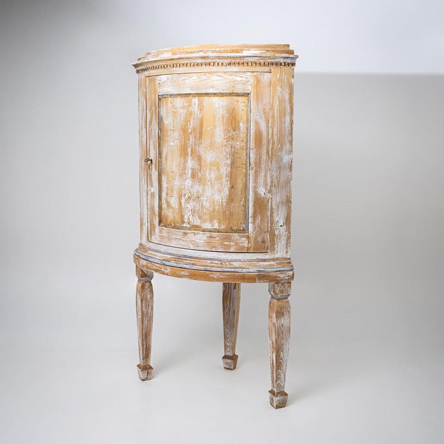 Semi-circular corner cabinet standing on four tapered legs with a molded apron and projecting cornice. The front with a...
