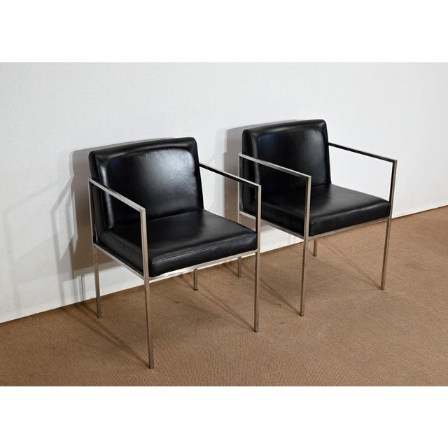 This pair of armchairs, with rectangular back and seat, in black imitation leather with stitching, has a brushed metal...