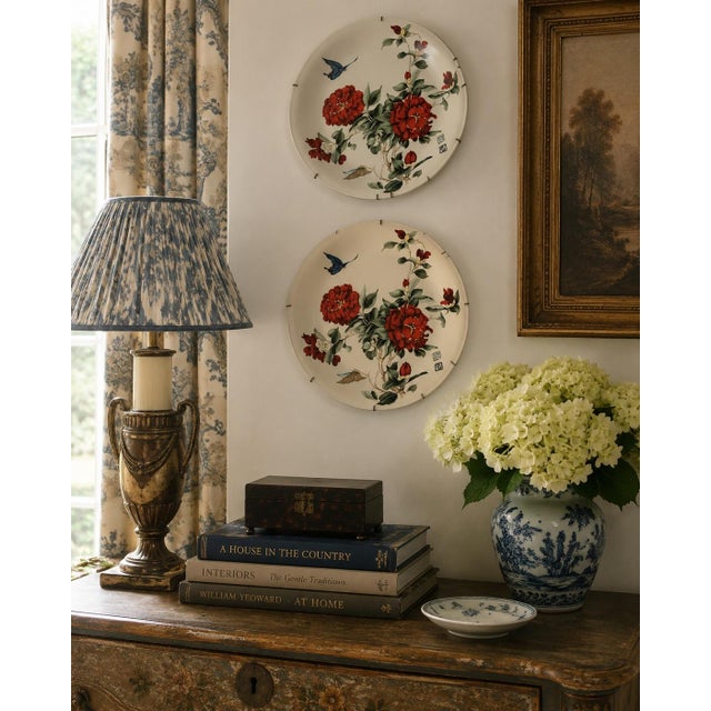 A charming pair of early 20th century Chinoiserie decorative wall plates, each painted with lush red blossoms, trailing...