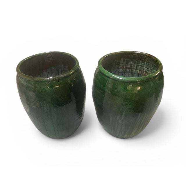 A pair of vintage ceramic pots features a rich, deep emerald green glaze with a high-gloss finish. The handcrafted nature...