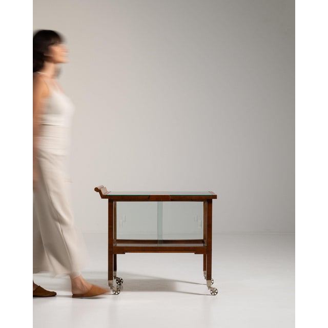 Glass-front walnut bar cart in Rich Walnut Brown. The rich walnut brown surface highlights glazed sliding doors, casters,...