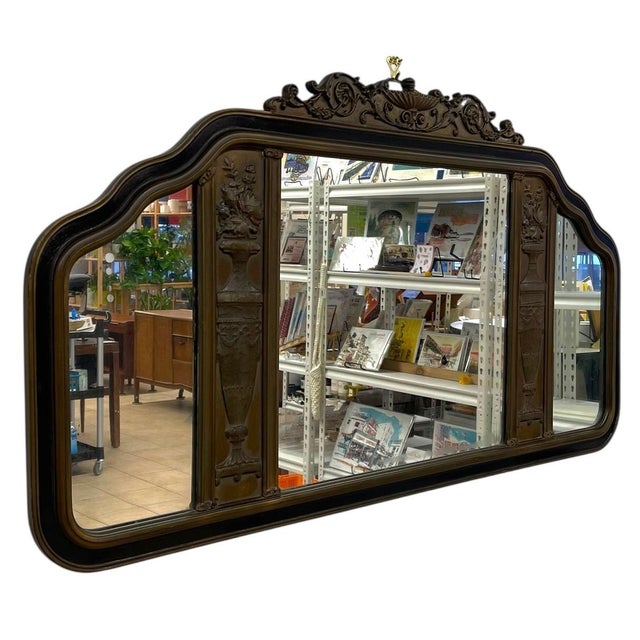 This antique overmantel mirror features an ornately carved wooden frame with a shaped, serpentine silhouette and richly...