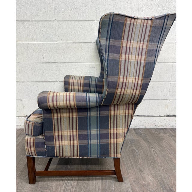 This is a vintage classic wingback armchair featuring a timeless plaid upholstery in muted blue, green, and burgundy...