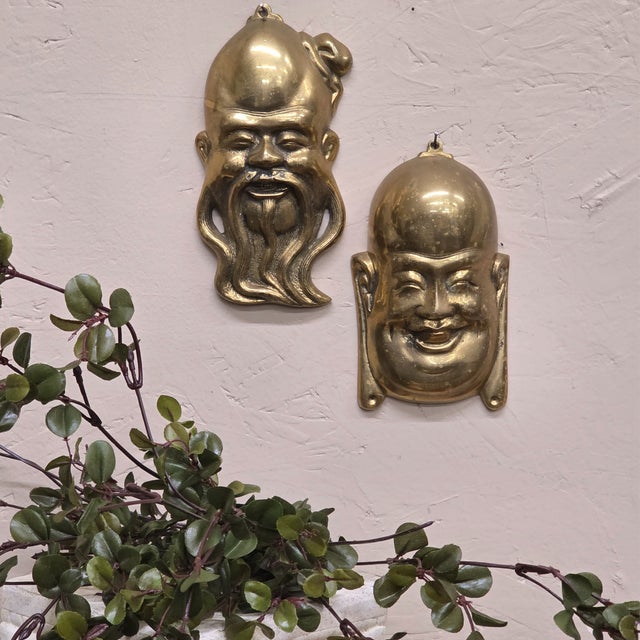 Sculptural vintage cast brass wall masks in a matching pair, featuring two expressive faces: one smiling figure and one...