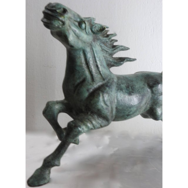 A stunning bronze horse figure showcases a beautiful patina. The figure depicts a horse in the midst of running with its...