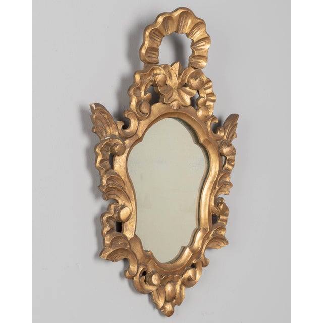 A French Baroque style giltwood mirror with cartouche shape framed by undulating borders. Hand-carved solid wood with...