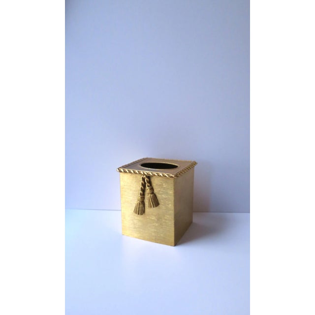 A gold metal tissue box cover with twist design around edge and tassel detail, circa mid to late-20th century, USA. Piece...