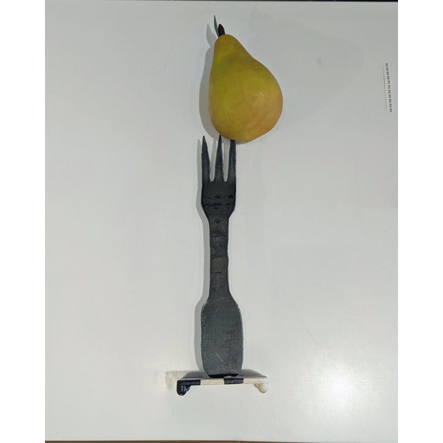Late 20th-century sculpture in forged iron, skewering a painted pear atop checkerboard base. Graphic and playful,