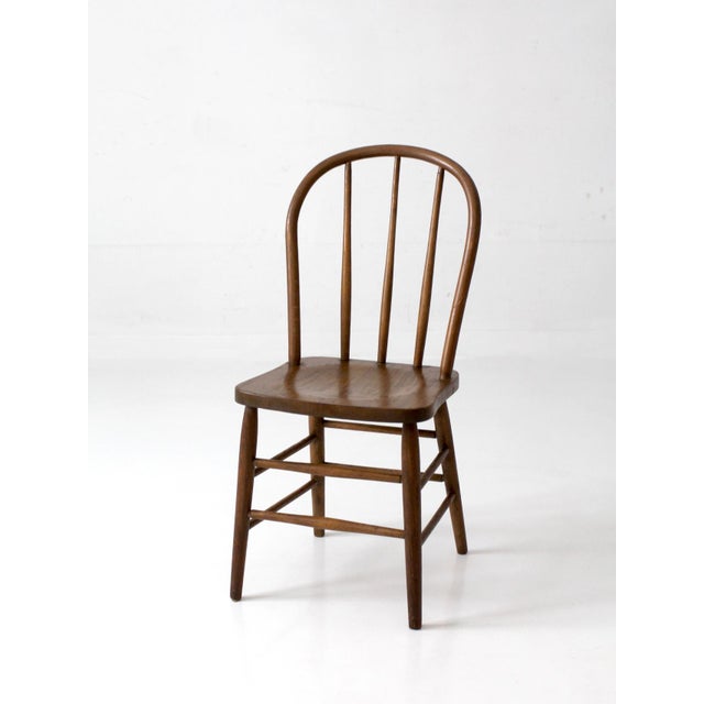 A vintage Windsor style bow back dining chair with a classic Early American silhouette, featuring a curved spindle back,...
