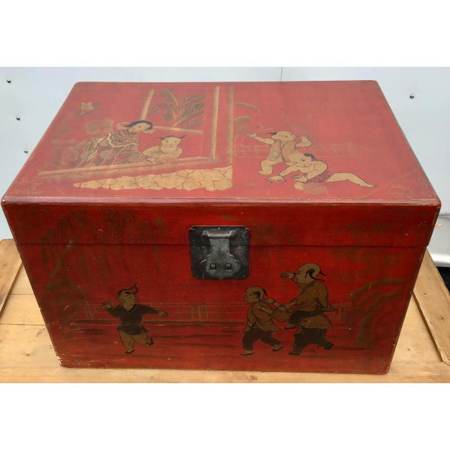 Asian style trunk with two side handles and center latch. Painted in a red lacquered chinoiserie finish with gold gilt...