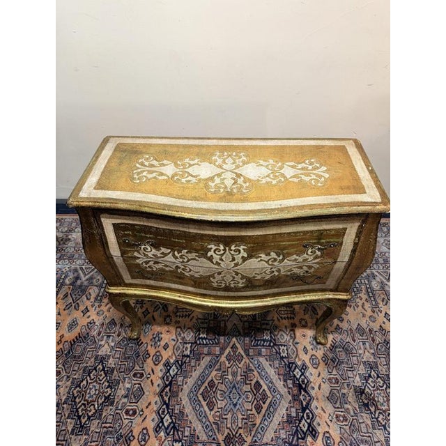 Striking bombe 2-drawer cabinet in Hollywood Regency style, featuring an ornate design with a beautiful gold and white...