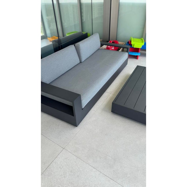 A confirmed Restoration Hardware outdoor pair: an architectural aluminum sofa with the signature open arm-shelf detail,...