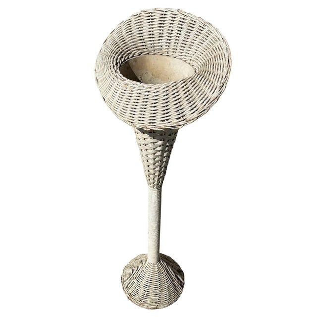 Whited painted wicker and rattan plant stand features a beautifully hand-woven, oversized plant holder supported by a...