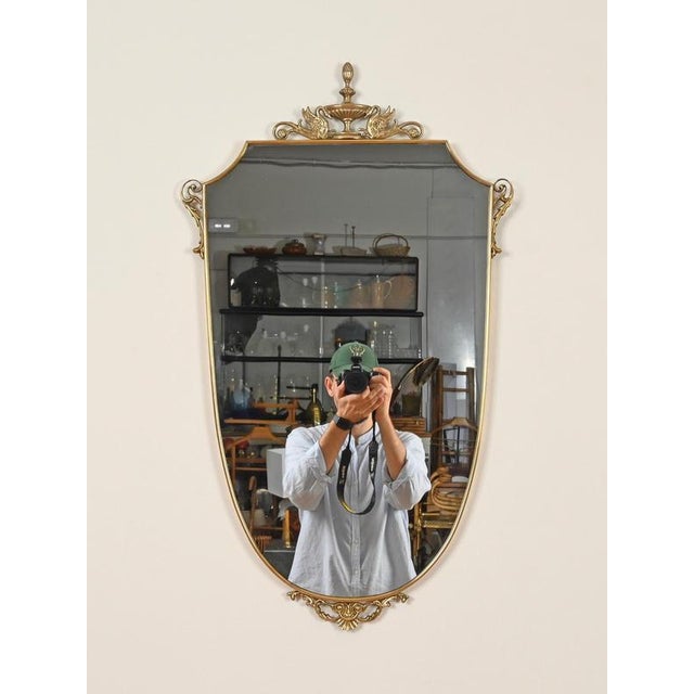 Wonderful and unique Mid-Century wall mirror in solid brass with an elegant shield-shaped silhouette. This refined mirror...