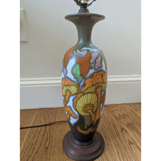 This table lamp features a base in the style of antique Dutch Gouda pottery from the 1920s, decorated with a vibrant,...