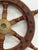 Small decorative ship’s wheel made of stained wood with turned handles and brass-tone center hub. Classic nautical design...