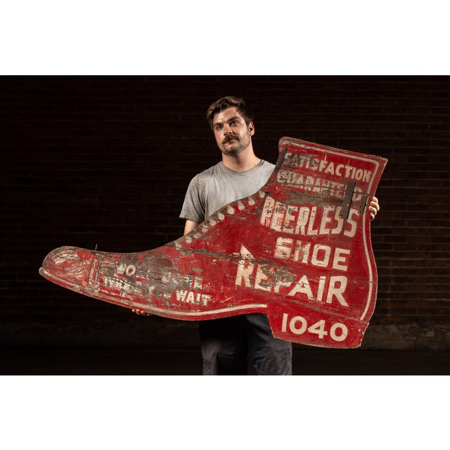 A monumental, boot-shaped wooden trade sign for Peerless Shoe Repair, painted in strong roadside red with white block...