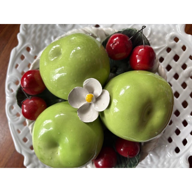hand-painted majolica set features a vibrant bowl of life-sized green apples, cherries, and a delicate white blossom, all...